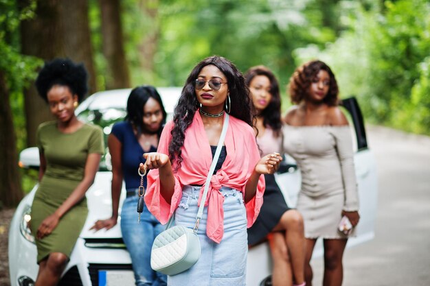 Groep van vijf gelukkige Afro-Amerikaanse meisjes poseerden tegen auto, een van hen toont sleutels