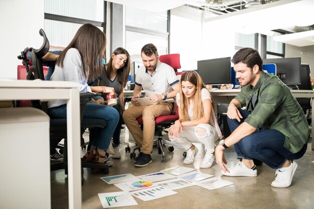 Groep van vijf zakenmensen die grafieken bekijken die op de kantoorvloer liggen