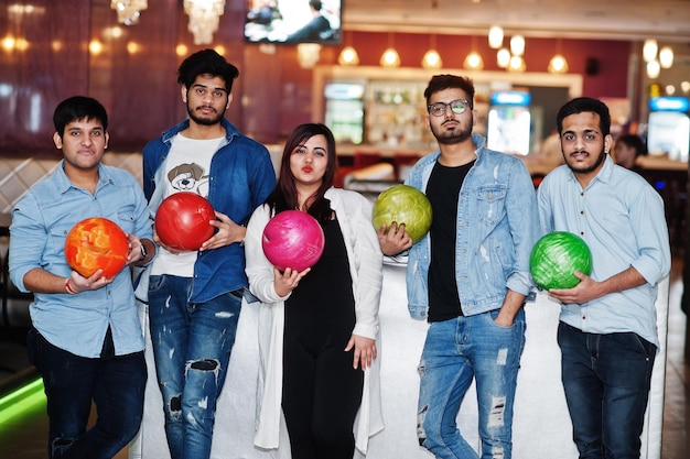 Groep van vijf Zuid-Aziatische volkeren die rust en plezier hebben in de bowlingclub met ballen bij de hand