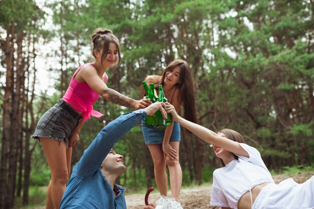 Groep vrienden die bierflessen rammelen tijdens picknick in de zomerbos