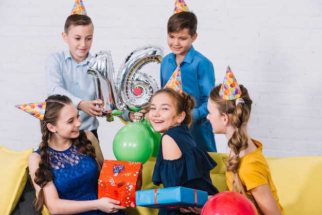 Groep vrienden die de verjaardag vieren door cadeaus te geven en strook nummer 16 folieballon te houden