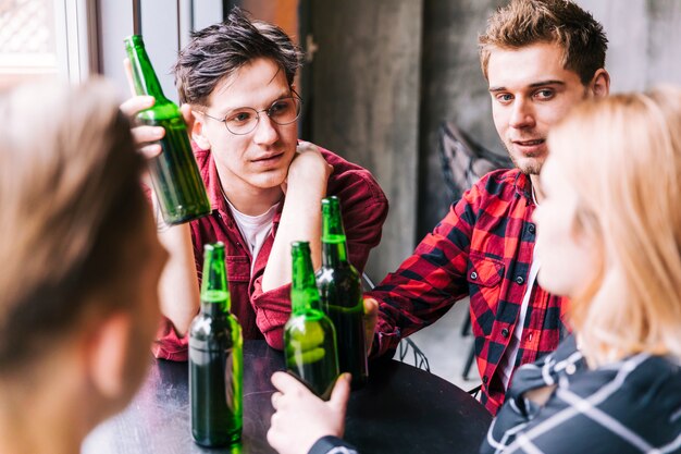 Groep vrienden die samen groene bierflessen zitten houden