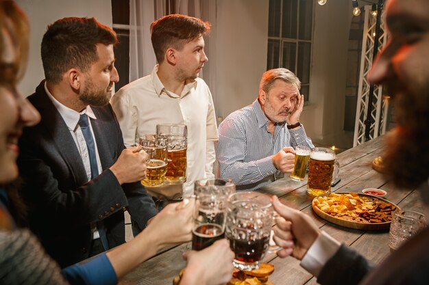 Groep vrienden genieten van 's avonds drankjes met bier op houten tafel