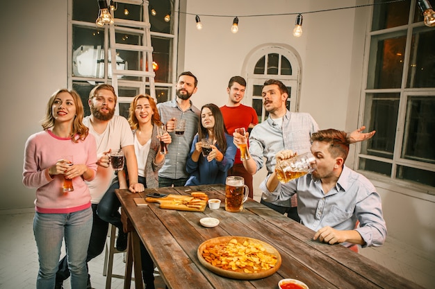Groep vrienden genieten van 's avonds drankjes met bier op houten tafel