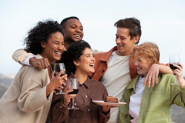 Groep vrienden poseren met glazen wijn en cake tijdens buitenfeest