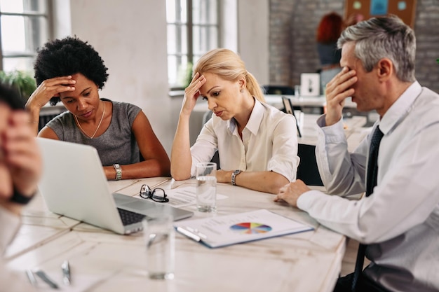 Groep zakencollega's die hoofdpijn hebben tijdens het werken op een laptop en proberen de problemen op te lossen tijdens een vergadering
