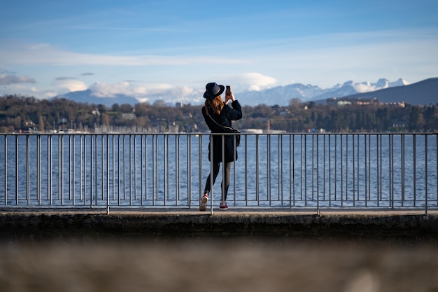 Groothoekopname van een vrouw die voor het water staat en foto's maakt van de bergen