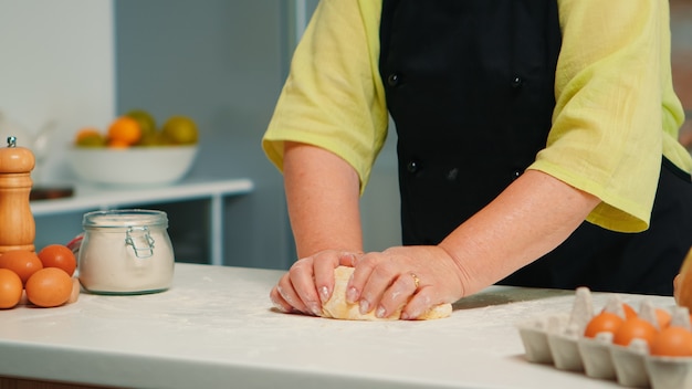 Grootmoeder handen bereiden zelfgemaakte koekjes in moderne keuken kneden op tafel. Gepensioneerde bejaarde bakker met bonete die ingrediënten mengt met tarwemeel voor het bakken van traditionele cake en brood