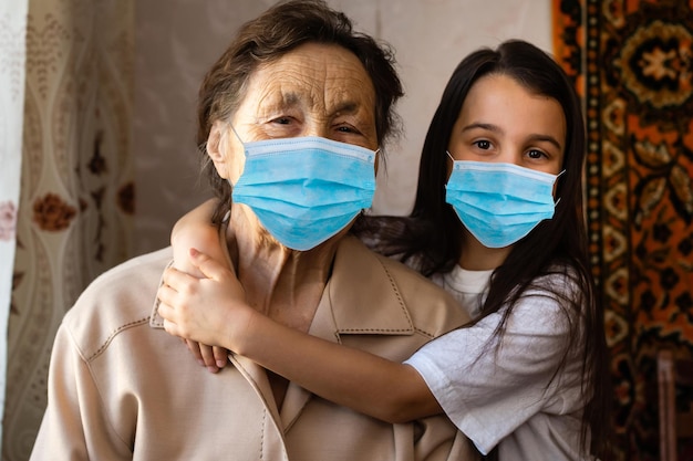 Grootmoeder met kleinkind in een masker speelt bij het raam van zijn huis. Blijf thuis. Quarantaine. Coronavirus (COVID-19.