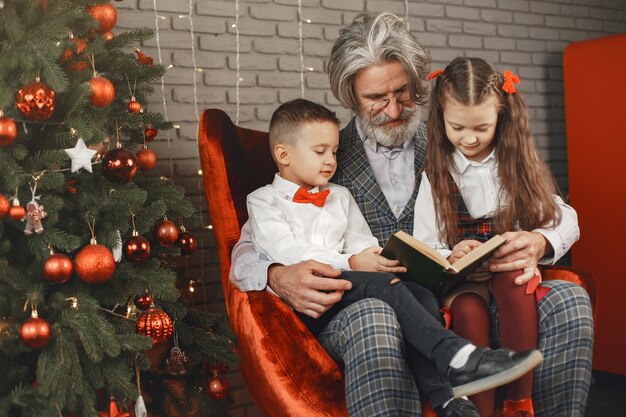 Grootvader draagt een bril, leest een boek voor kleine kleindochters tweeling in een kamer ingericht voor Kerstmis. Kerst vakantie concept. contrast fotografie