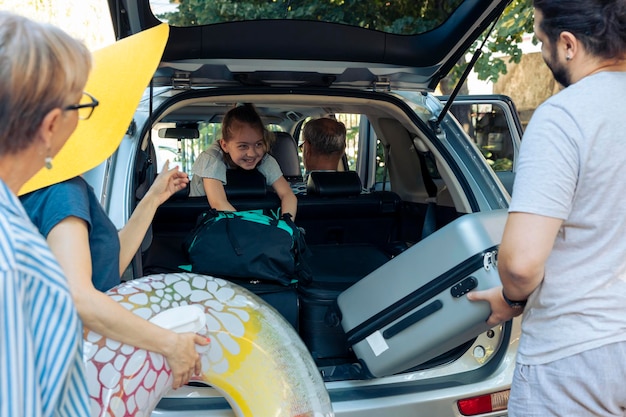 Grote europese familie die op vakantie reist, trolleytassen en opblaasbaar laadt om op zomervakantie te vertrekken. Ouders met klein kind en grootouders gaan op avontuurlijke reis met voertuig.