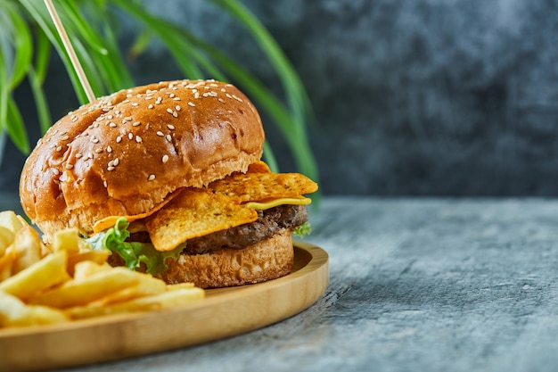 Grote hamburger met gebakken aardappel in de houten plaat op het marmeren oppervlak