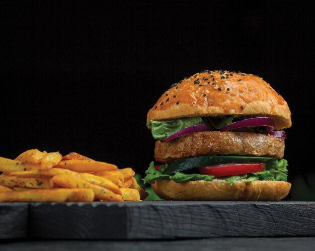 Grote mac-hamburger en aardappels stokken op een donkere houten bord.