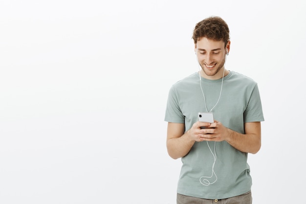 Guy luisteren muziek in oortelefoons. Portret man in t-shirt, smartphone houden en glimlachend op scherm