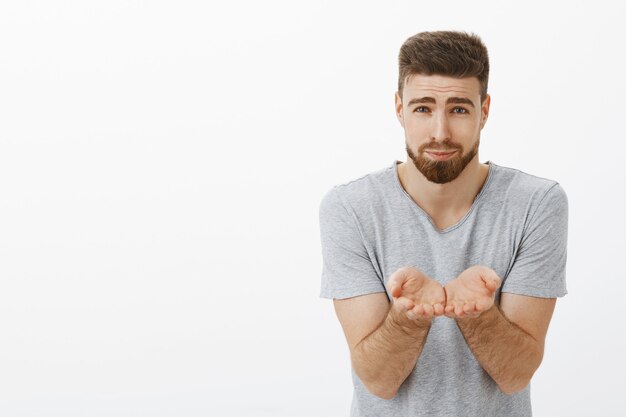 Guy suggereert dat zijn hart een aardig en schattig vriendje is. Charmante knappe en mannelijke blanke donkerbruine handpalmen bij de borst alsof ze iets breekbaars in de armen dragen dat over een grijze muur staat