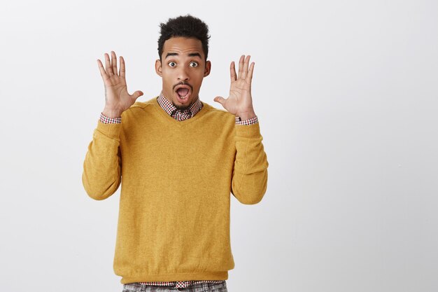 Guy was bang van een onverwachte knal. Portret van aantrekkelijke grappige Afro-Amerikaan met afrokapsel die palmen dichtbij gezicht opheft, schreeuwend van verbazing en verbazing, kaak laat vallen en hijgend