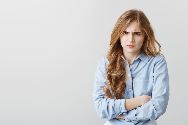 Haat je, praat niet tegen me. Portret van beledigde schattige Europese vrouw met blond haar, hand in hand op de borst gekruist, fronsend, teleurgesteld en verdrietig van belediging, staande over grijze muur