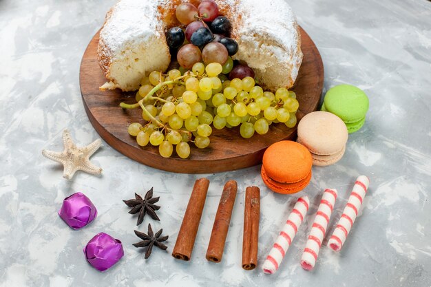 Half-bovenaanzicht suiker poedervormige cake met druiven kaneel en macarons op witte oppervlakte suiker cake zoete bak koekje