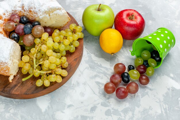 Half-bovenaanzicht suiker poedervormige cake met verse druiven en appels op wit bureau fruit cake koekje zoete suiker bakken