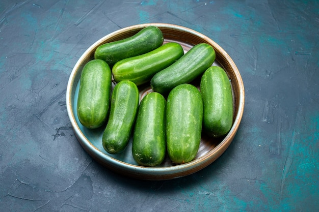 Half-bovenaanzicht verse groene komkommers rijpe groenten in plaat op donkerblauw bureau.