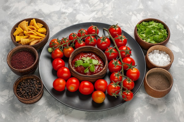 Half-bovenaanzicht verse kerstomaatjes in plaat met tomatensaus en verschillende kruiden op witte ondergrond