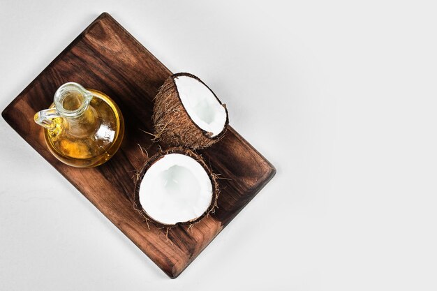 Half gesneden kokosnoot en fles olie op een houten bord.