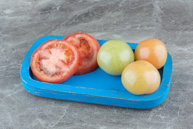 Half gesneden rijpe tomaat met onrijpe groene tomaten op blauwe houten plaat.