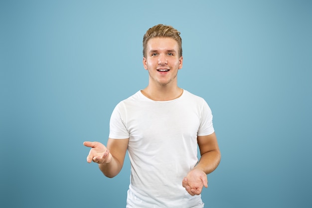 Half-length portret van een blanke jonge man op blauwe studio achtergrond. Mooi mannelijk model in overhemd. Concept van menselijke emoties, gezichtsuitdrukking, verkoop, advertentie. Iets wijzen en laten zien.