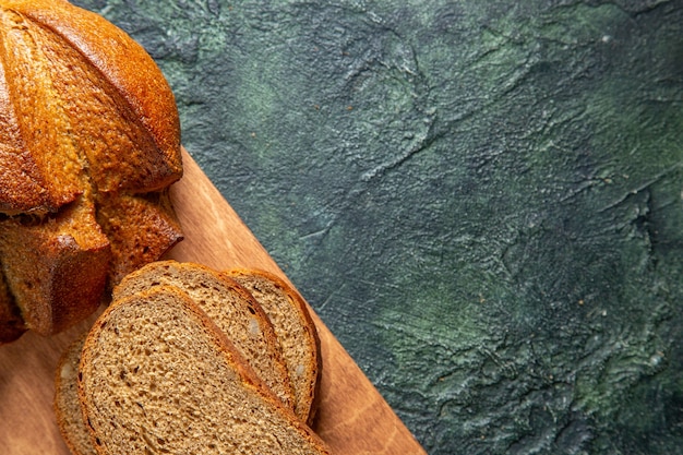 Half schot van geheel en gesneden zwart brood op bruine houten snijplank op donkere kleuren achtergrond