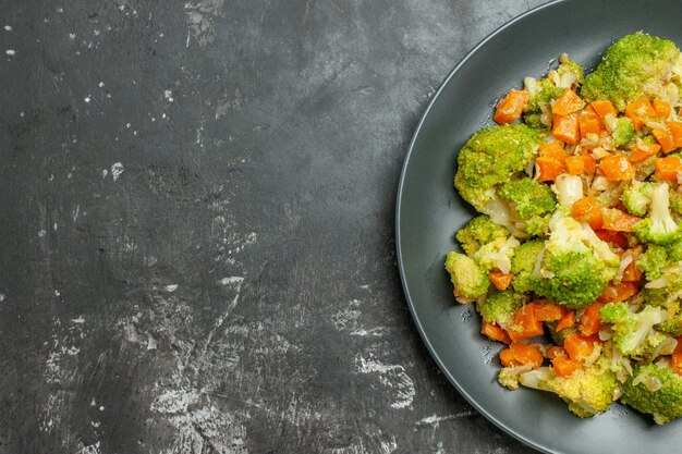 Half schot van gezonde maaltijd met brocoli en wortelen op een zwarte plaat op grijze tafel