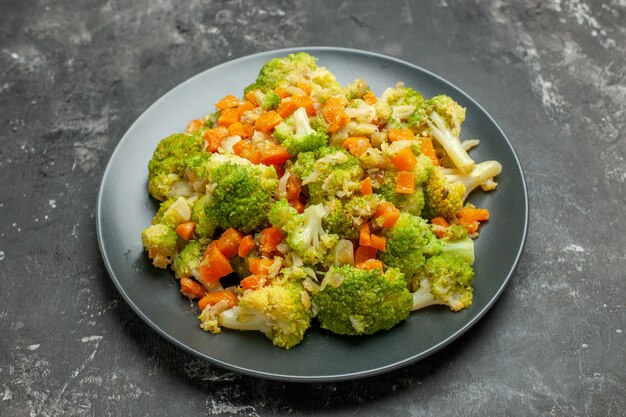 Half schot van gezonde maaltijd met brocoli en wortelen op een zwarte plaat op grijze tafel