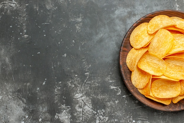 Half schot van heerlijke zelfgemaakte aardappelchips op een bruine plaat op grijze tafel