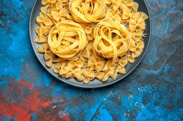 Half shot van de voorbereiding van het diner met pasta noedels op een zwarte plaat aan de linkerkant op blauwe achtergrond