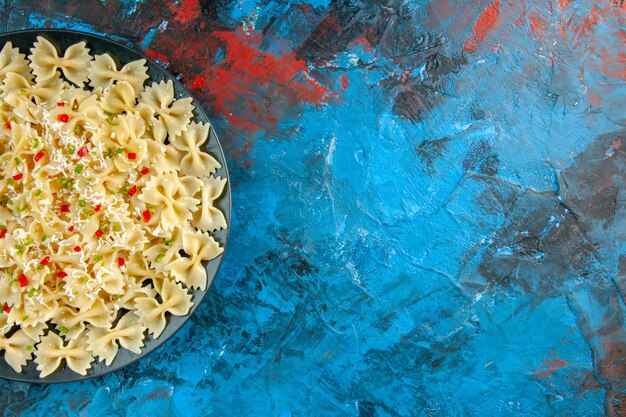 Half shot van rauwe Italiaanse farfalle pasta met groenten aan de rechterkant op blauwe achtergrond