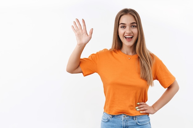 Hallo buurman. Glimlachend blond meisje dat thuis bij het raam staat tijdens zelfquarantaine en haar vriend aan de overkant zwaait om gedag te zeggen