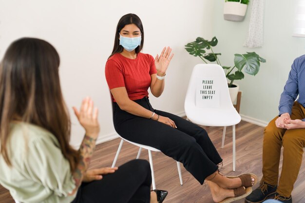 Hallo vriend! Gelukkige jonge vrouw die een gezichtsmasker draagt dat zwaait en hallo zegt tegen een lid van haar steungroep