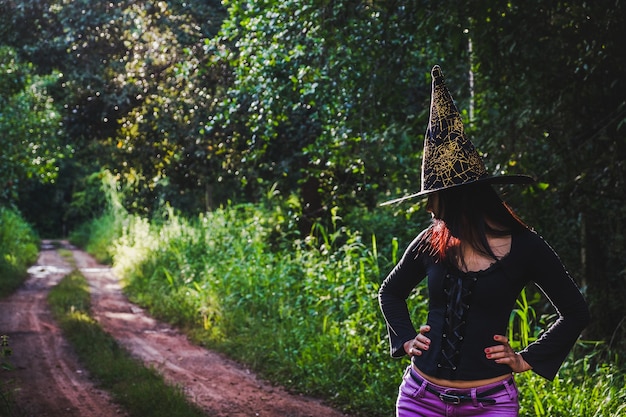 Halloween-kunstontwerp, mooie jonge vrouw in heksenhoed in het bos