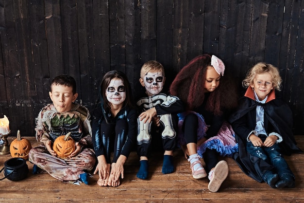Gratis foto halloweenfeest met groep kinderen die samen op een houten vloer in een oud huis zitten.