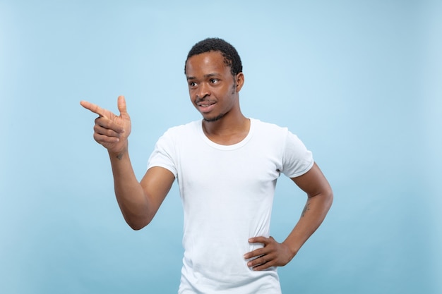 Halve lengte close-up portret van jonge Afro-Amerikaanse man in wit overhemd op blauwe ruimte