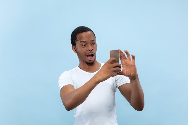 Halve lengte close-up portret van jonge Afro-Amerikaanse man in wit overhemd op blauwe ruimte