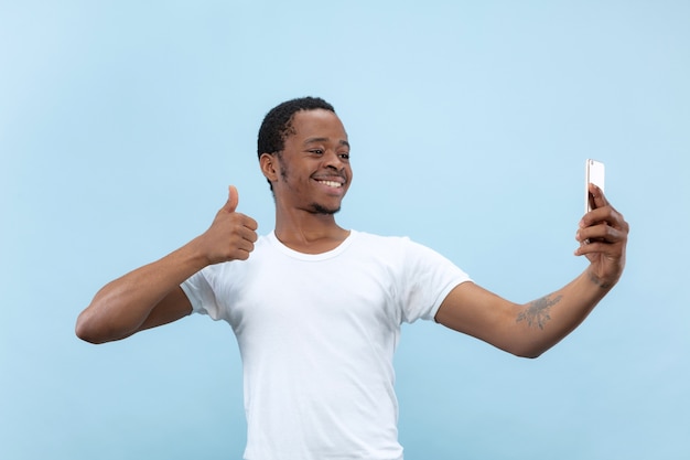 Halve lengte close-up portret van jonge Afro-Amerikaanse man in wit overhemd op blauwe ruimte