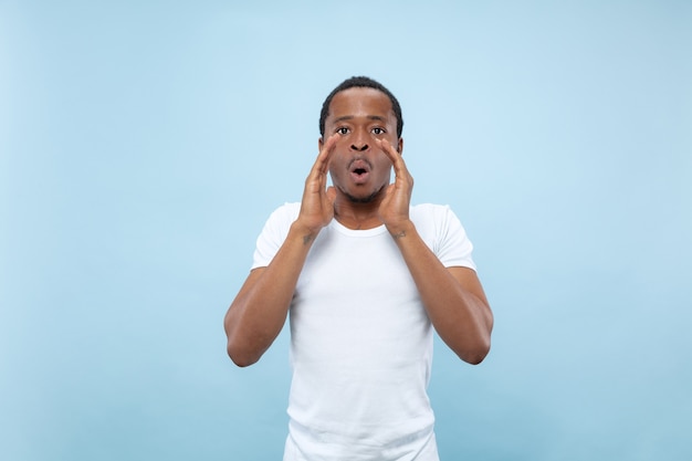 Halve lengte close-up portret van jonge Afro-Amerikaanse man in wit overhemd op blauwe ruimte