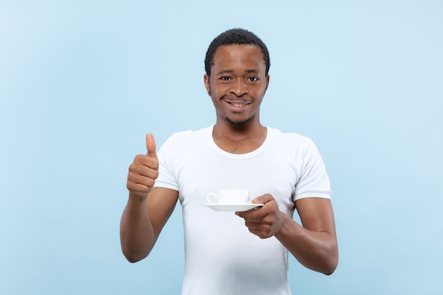 Halve lengte close-up portret van jonge Afro-Amerikaanse man in wit overhemd op blauwe ruimte