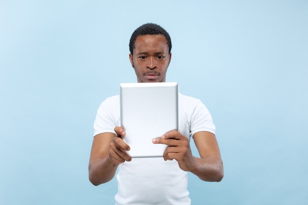 Halve lengte close-up portret van jonge Afro-Amerikaanse man in wit overhemd op blauwe ruimte