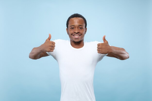 Halve lengte close-up portret van jonge Afro-Amerikaanse mannelijk model in wit overhemd op blauwe studio achtergrond. Menselijke emoties, gezichtsuitdrukking, advertentieconcept. Het teken van OK laten zien. leuk.