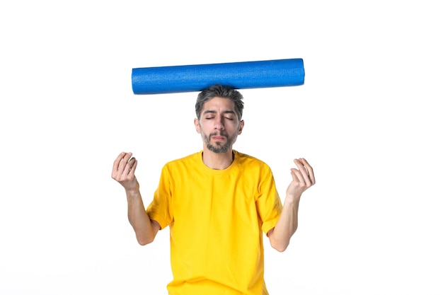 Halve lichaamsopname van een dromerige jongeman in een geel shirt en met een gevouwen blauwe mat op zijn hoofd op een witte achtergrond
