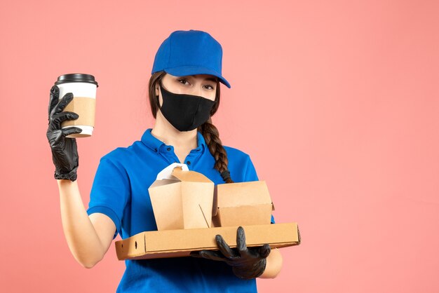 Halve lichaamsopname van een hardwerkend koeriersmeisje met een medisch masker en handschoenen met bestellingen op een pastelkleurige perzikachtergrond