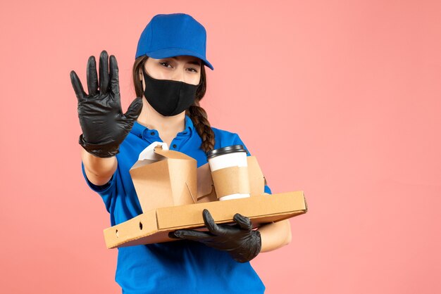 Halve lichaamsopname van koeriersmeisje met een medisch masker en handschoenen met bestellingen met vijf op pastelkleurige perzikachtergrond