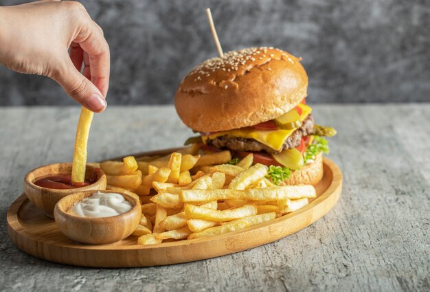 Hamburger en gebakken aardappelen in een houten schotel met sauzen