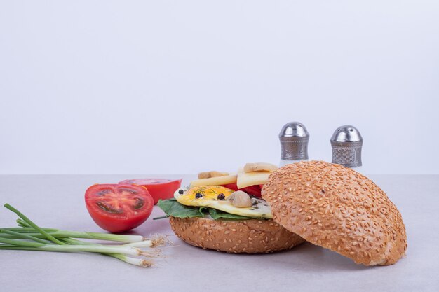 Hamburger met omelet, tomaten, champignons en ui op een witte ondergrond.